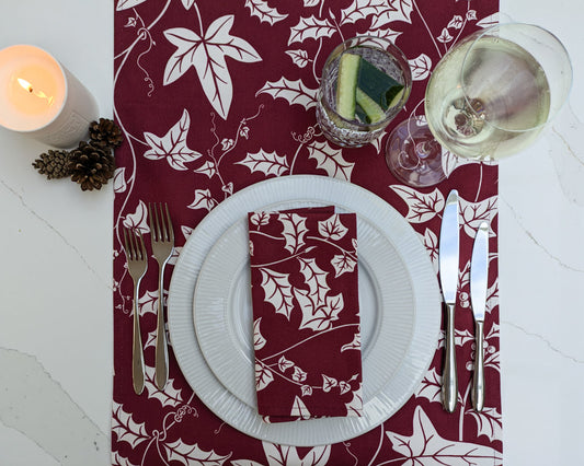 Holly and Ivy Burgundy table runner and napkin on a festive laid marble tabletop