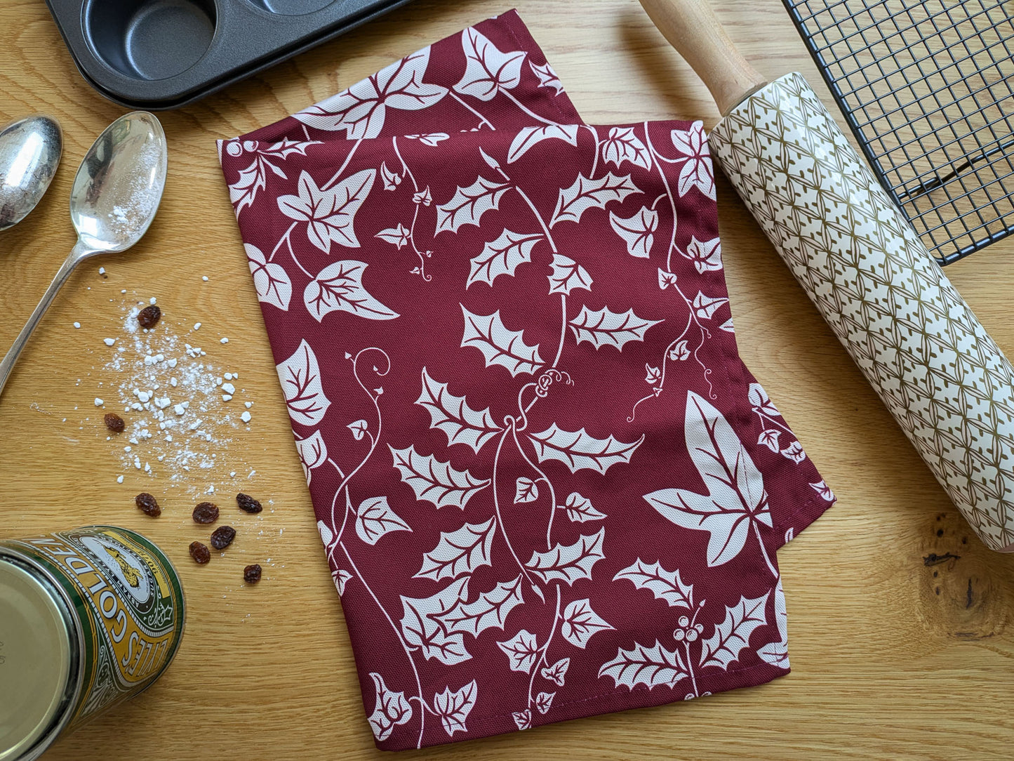 Christmas foliage patterned tea towel shown with baking equipment and ingredients
