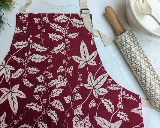 Holly and Ivy Botanical illustrated kitchen apron on a marble surface with patterned rolling pin and baking equipment