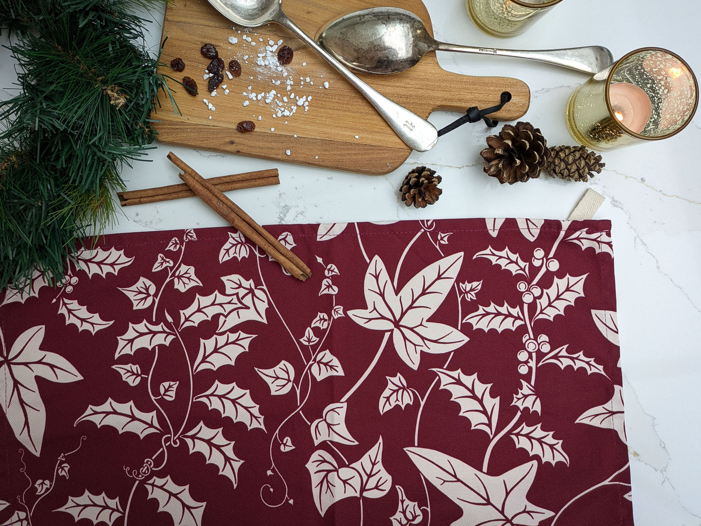 Christmas patterned tea towel on a marble worktop with Christmas candles, pine cones and baking ingredients