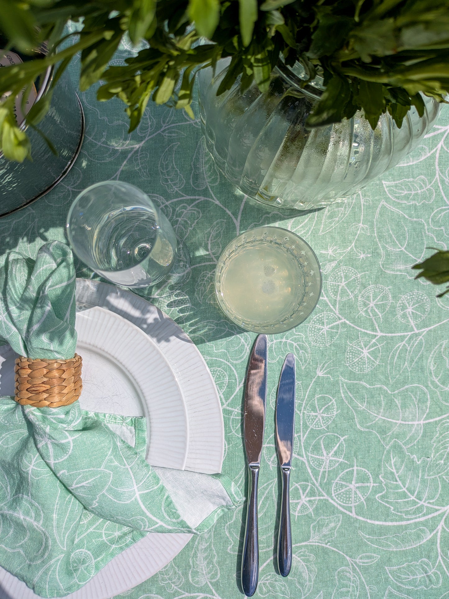 Close up of soft green tomato tablecloth with flowers, plates, cutlery and glasses laid