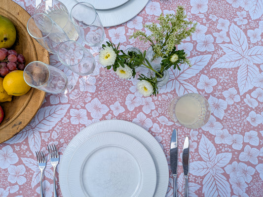 Table setting with white plates, silverware, a floral tablecloth and fresh fruit with cut buds