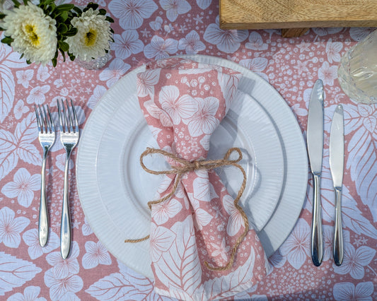 Inviting dinner setting with white plates, silverware, and a soft pink hydrangea floral tablecloth and napkin