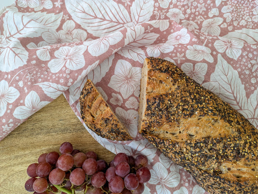 Loaf of bread and bunch of grapes on a wooden board with soft pink floral-patterned tea towel