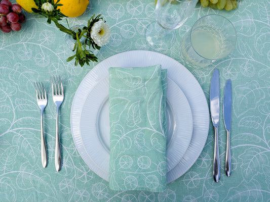 Table setting with white plates, silverware, and a green patterned napkin on a teal tablecloth.