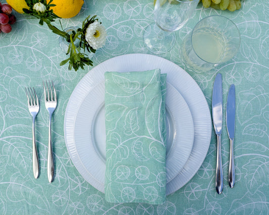 Table setting with white plates, silverware, and a green patterned napkin on a teal tablecloth.