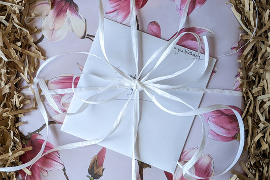 Beautifully wrapped gift in Magnolia pink wrapping paper with hand written card and white raffia ribbon packaged up with shredded kraft paper to send