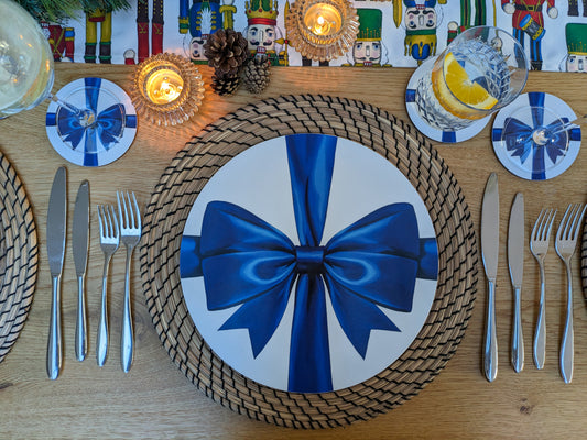 Christmas decorative table setting with a blue bow on a plate, surrounded by cutlery and candles.