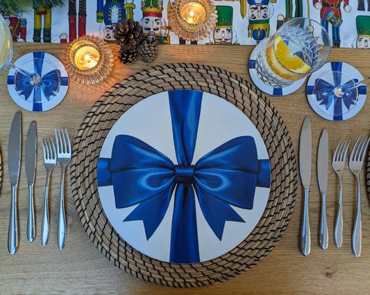 Christmas decorative table setting with a blue bow on a plate, surrounded by cutlery and candles.