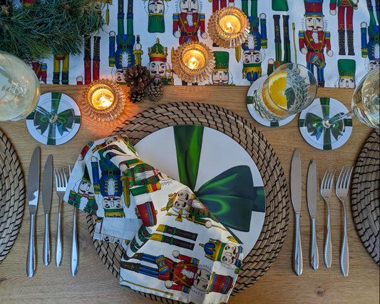 Nutcracker illustrated table runner and napkins shown on a dressed Christmas table with ribbon tableware, lit candles and festive foliage