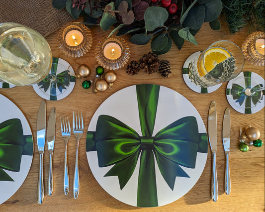Decorative table setting with green bow placemats, candles, and glasses on a wooden table.