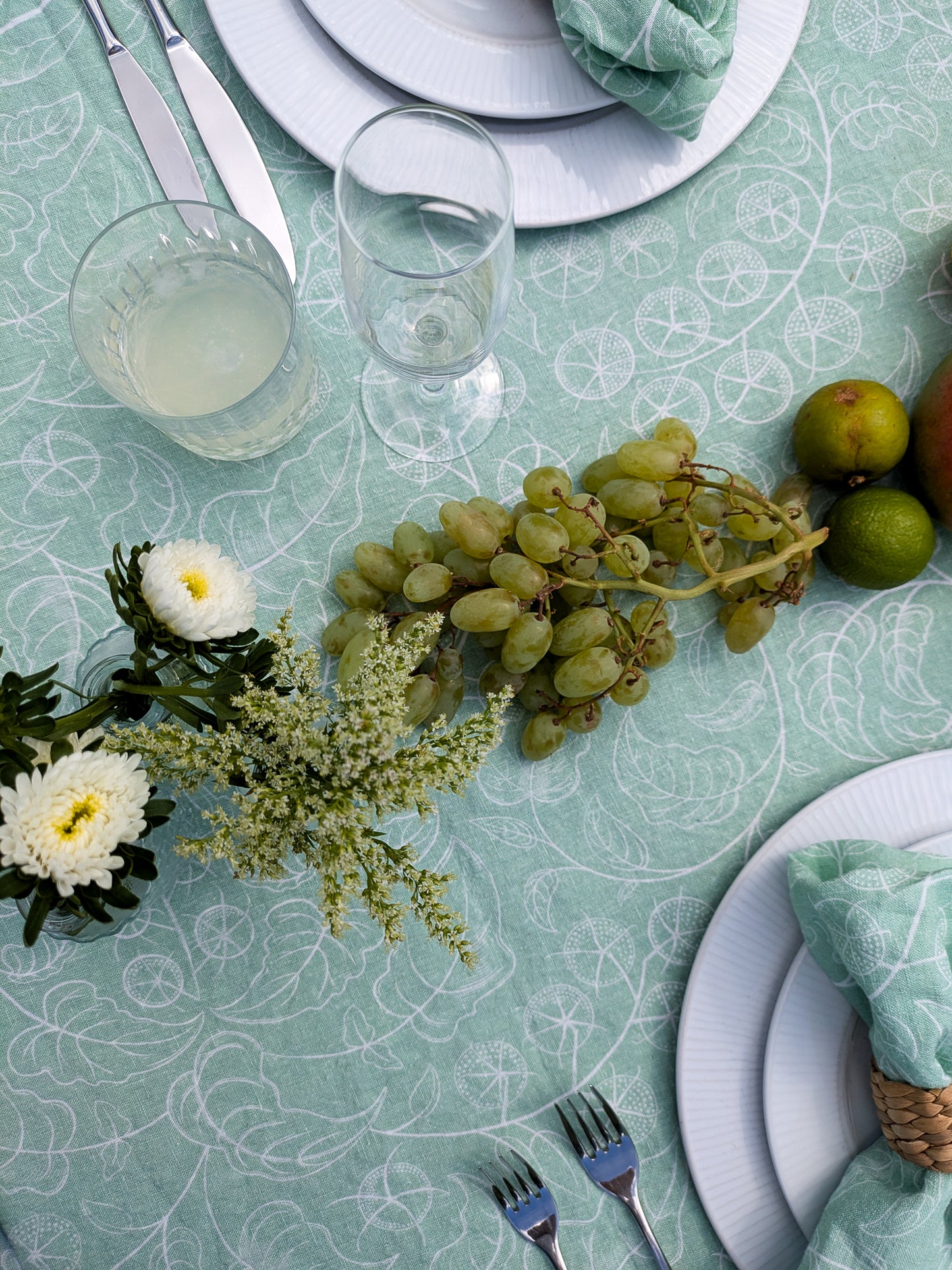 Elegant table setting with green grapes, white flowers, and silverware on a soft pastel patterned table cloth