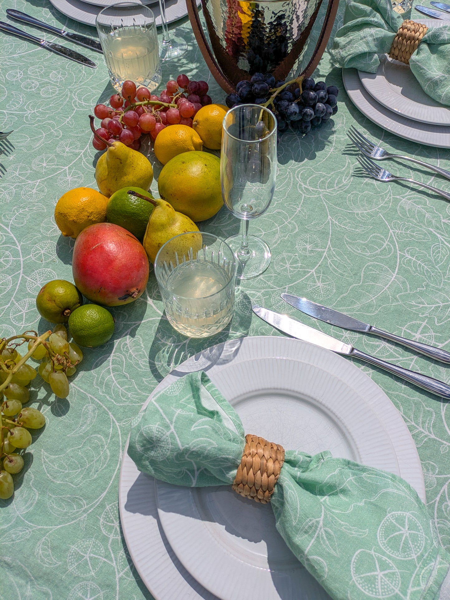 Table setting with fruit, glasses, and cutlery on a green tomato patterned table cloth