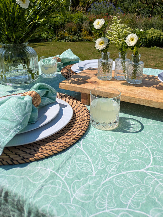 Outdoor table setting with green tomato tablecloth, full glasses, floral arrangement and inviting setting