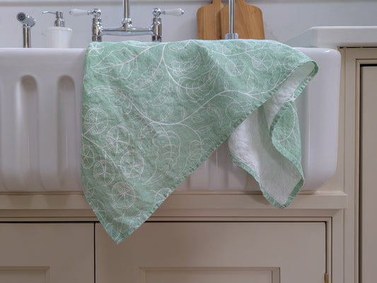 Green tomato vine patterned towel draped over a white sink in a modern country kitchen setting