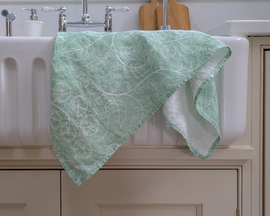 Green tomato vine patterned towel draped over a white sink in a modern country kitchen setting