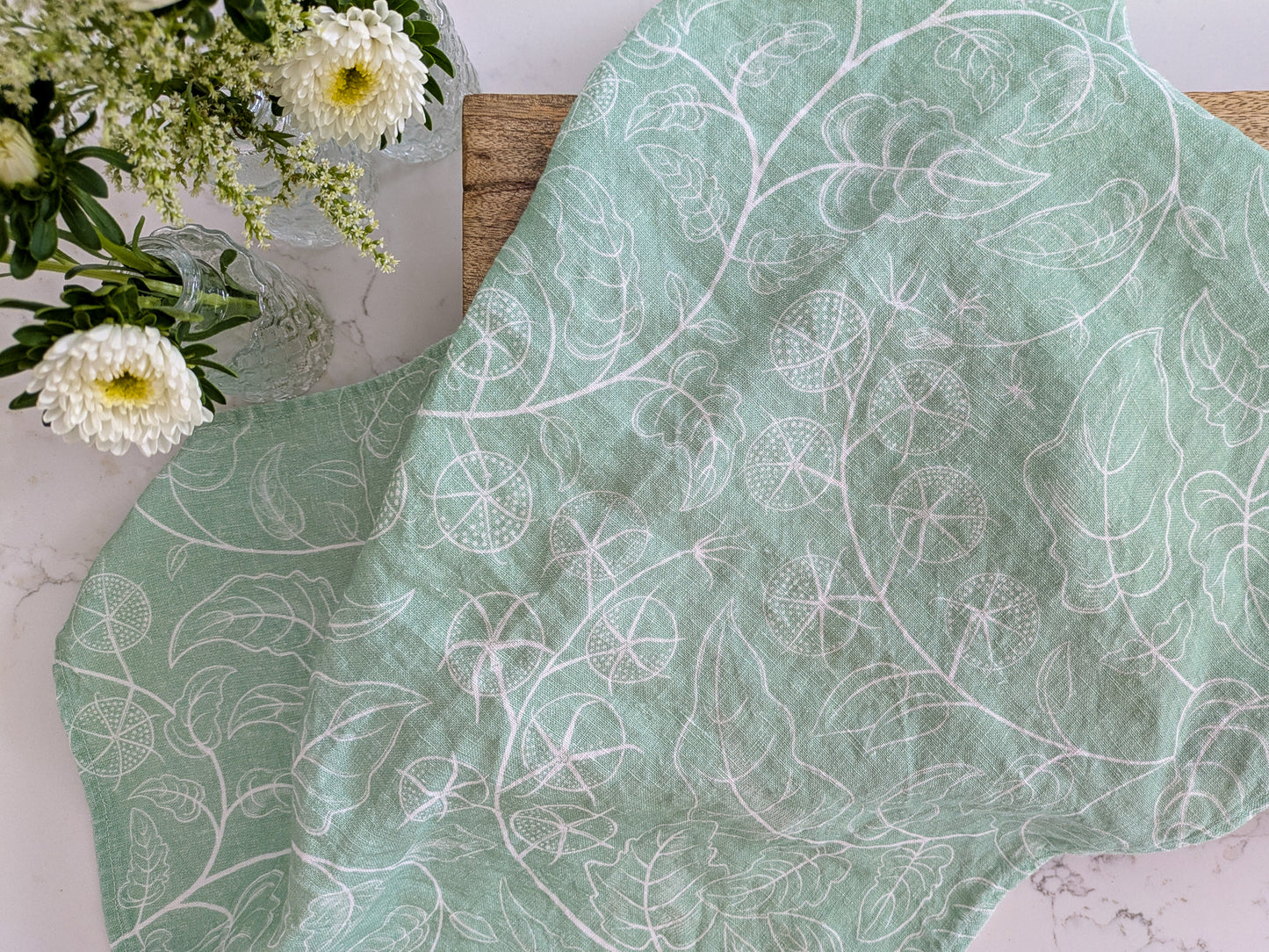 Soft green tomato tea towel with white pattern on a marble surface and fresh cut flowers