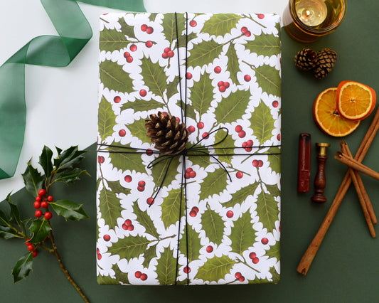 Holly and berry illustrated wrapping paper on a wrapped gift with seasonal foliage and wax seal