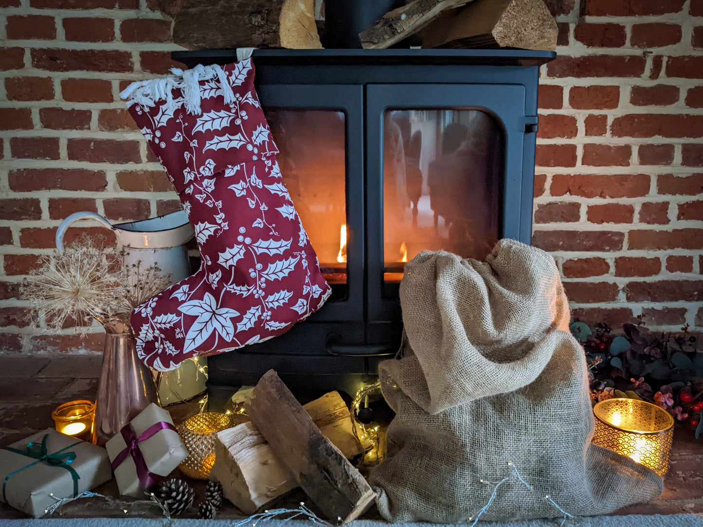 Warm cosy lit fireplace with logs, candles, presents and Catherine Jane Designs Holly and Ivy Christmas stocking hanging on the fire