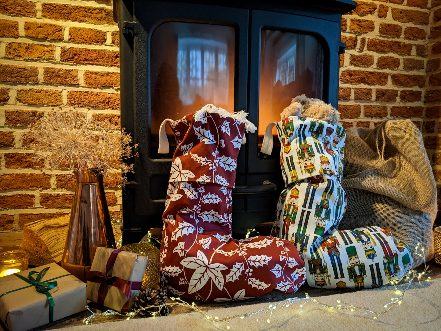 Full Holly and Ivy patterned stocking with filled Nutcracker patterned stocking propped up in the fireplace surrounded by gifts
