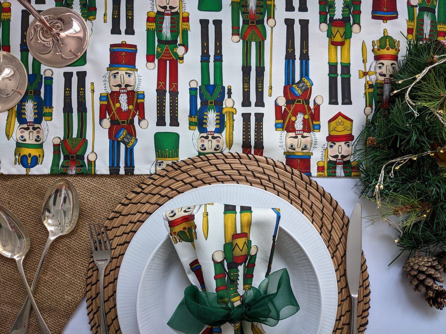 Close up of novelty nutcracker designed table runner and napkins, with party bow, fairy lights and silver goods