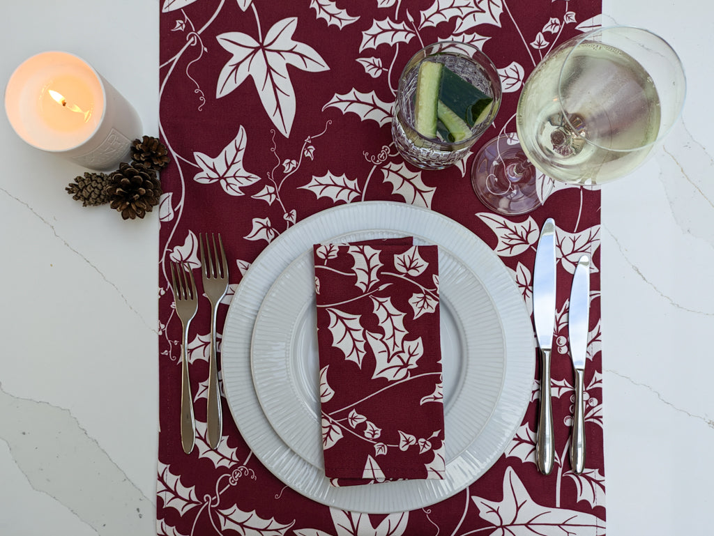 Holly and Ivy Burgundy table runner and napkin on a festive laid marble tabletop