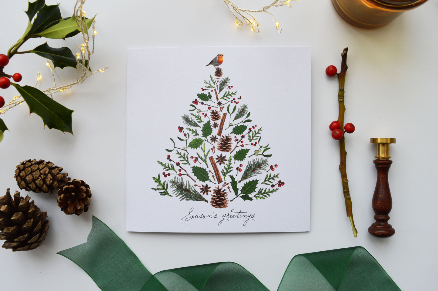 Christmas tree card with 'Season's greetings' message pictured with fairy lights, ribbon, pine cones and berries