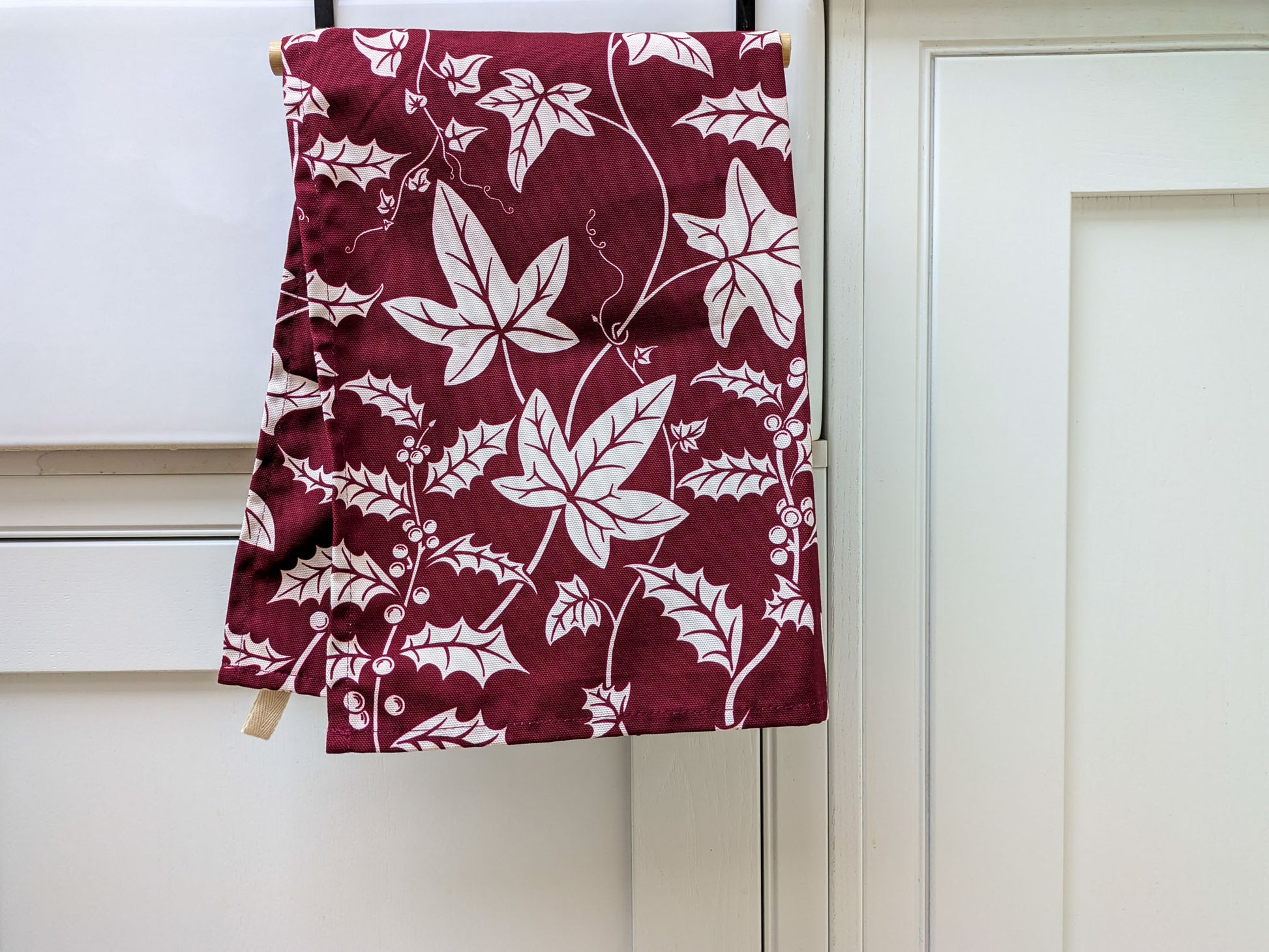 Holly and Ivy burgundy and white Christmas tea towel hanging in a fresh white kitchen