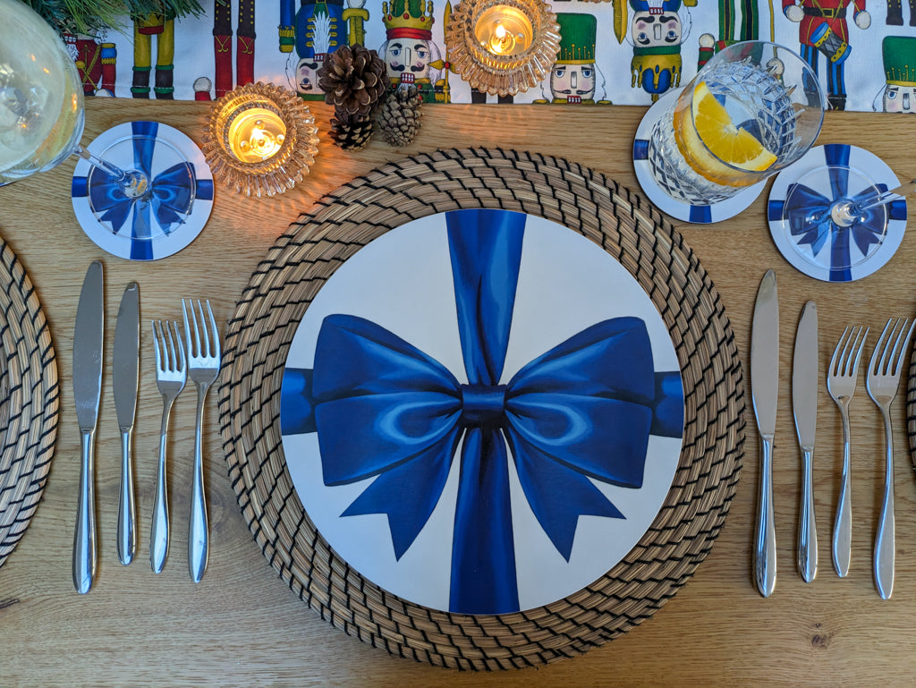 Christmas decorative table setting with a blue bow on a plate, surrounded by cutlery and candles.