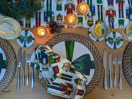 Nutcracker illustrated table runner and napkins shown on a dressed Christmas table with ribbon tableware, lit candles and festive foliage