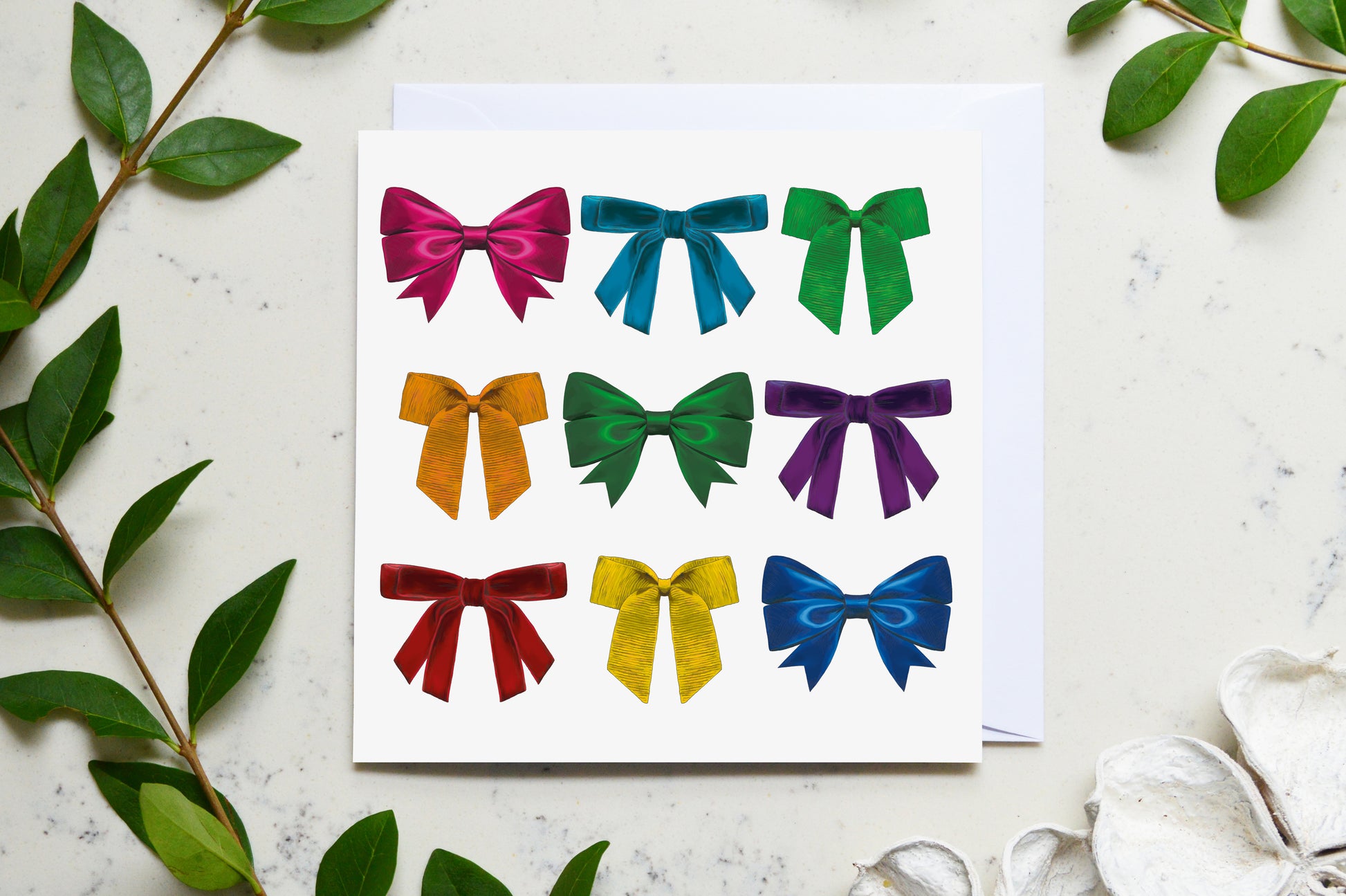 Bold and bright rainbow ribbon card pictured on a marble top with fresh foliage