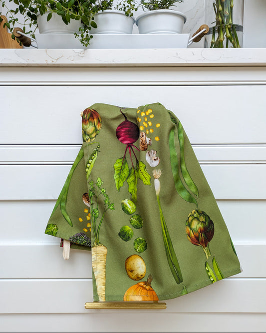 Styled sage green vegetable illustrated tea towel in crisp white kitchen with fresh herbs