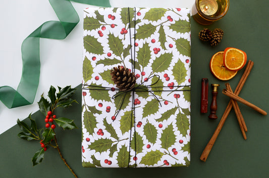 Holly and berry illustrated wrapping paper on a wrapped gift with seasonal foliage and wax seal