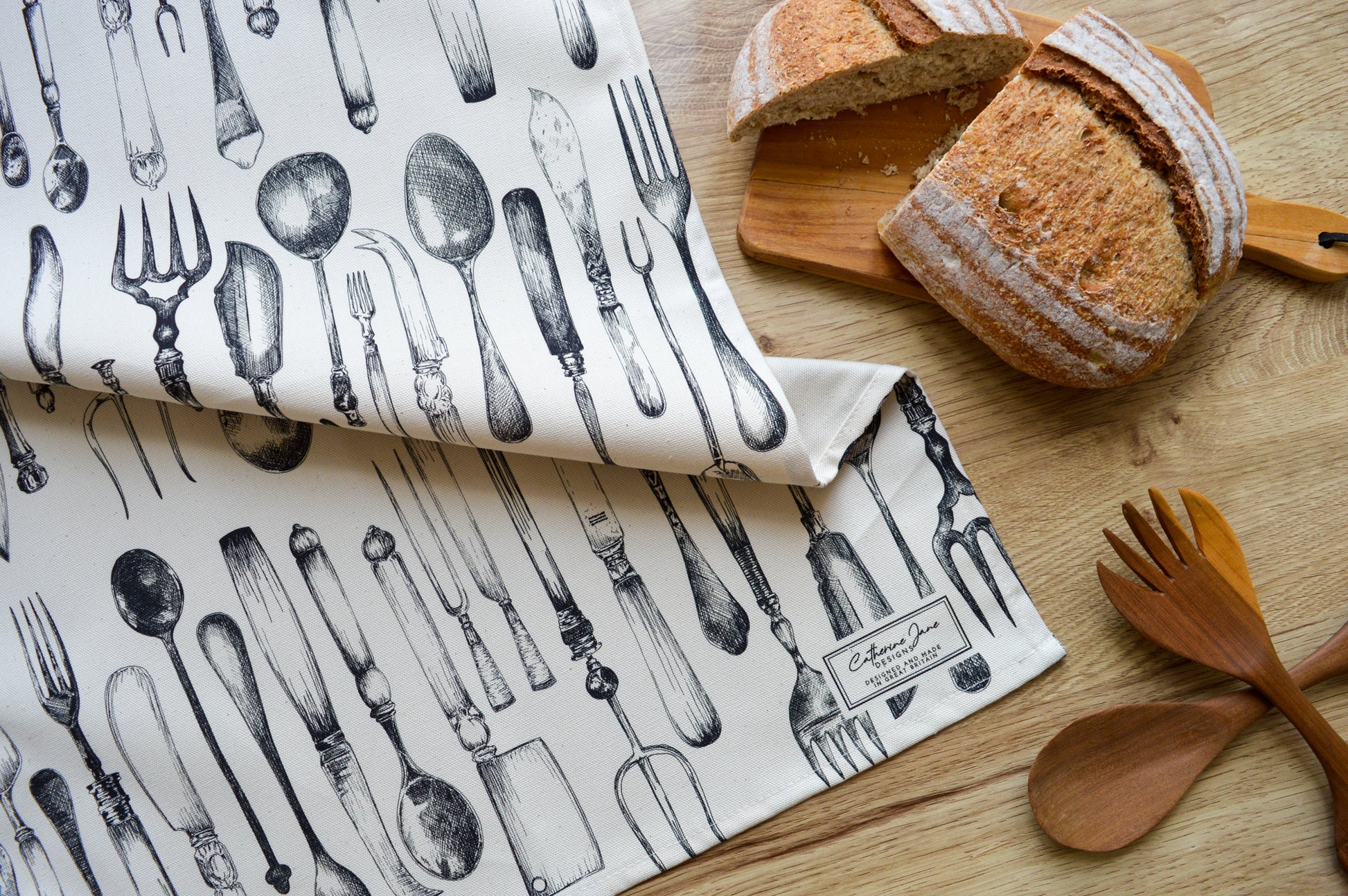 Knife, fork and spoon tea towel with freshly baked bread on a warm wooden worktop